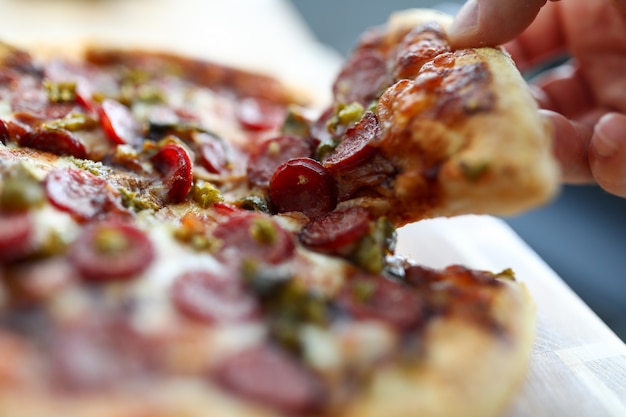 Male hand holding big piece of tasty fresh pizza close-up