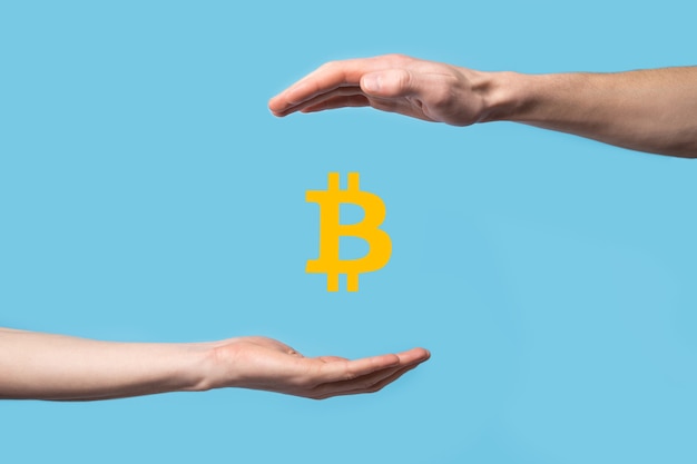 Male hand holding a bitcoin icon on blue surface