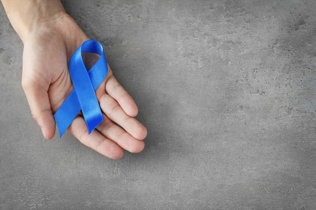 Male hand holding blue ribbon on grey. Prostate cancer concept