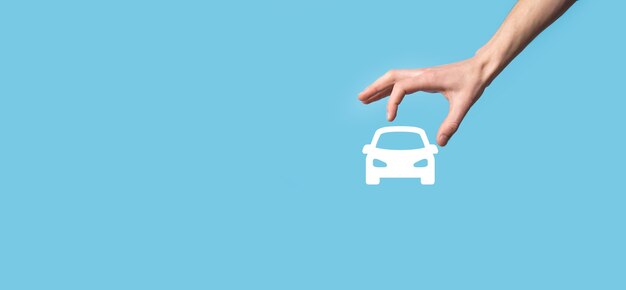 Male hand holding car auto icon on blue background. Wide banner composition.Car automobile insurance and collision damage waiver concepts.