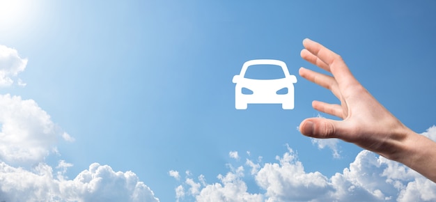 Male hand holding car auto icon on blue background. Wide banner composition.Car automobile insurance and collision damage waiver concepts.