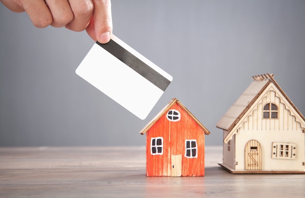 Male hand holding credit card with a house model on the wooden table.