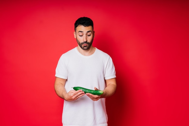 Male hand holding cucumber on red background space for text