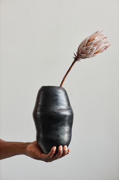 Male hand holding dark ceramic vase with exotic flower wabi\
sabi design