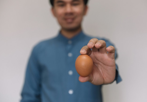 灰色の背景で隔離のイースター茶色の鶏卵を持っている男性の手