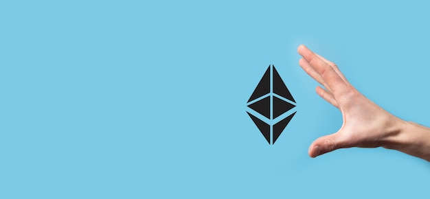 Male hand holding a Ethereum icon on blue background. Ethereum and cryptocurrency investing concept. exchanging, trading, transfer and investment of blockchain technology.