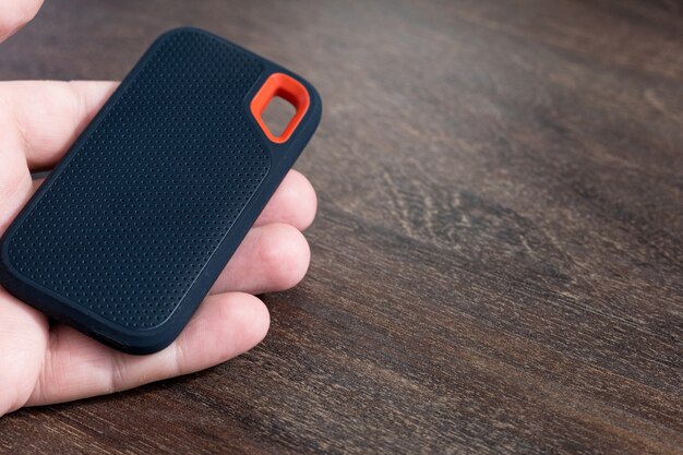 Male hand holding an external SSD Drive isolated on wooden background. Selective focus.