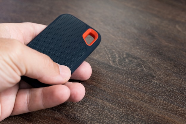 male hand holding an external ssd drive isolated on wooden background. selective focus.