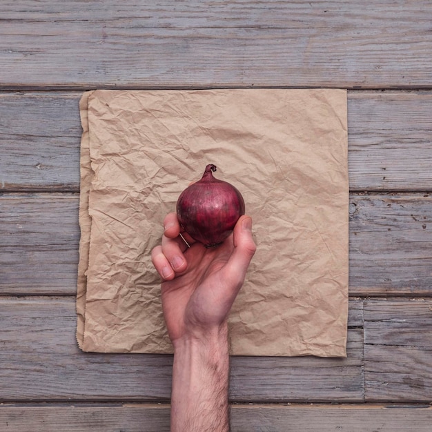 A male hand holding a fresh red onion against a rustic background