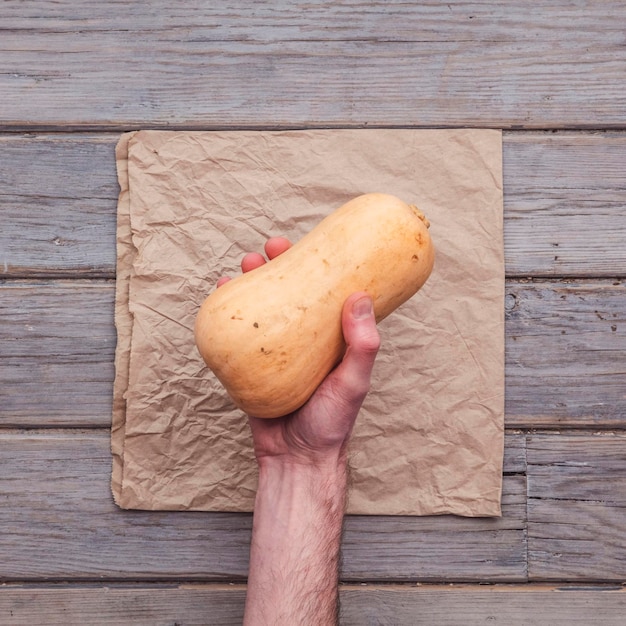 A male hand holding a fresh squash against a rustic background