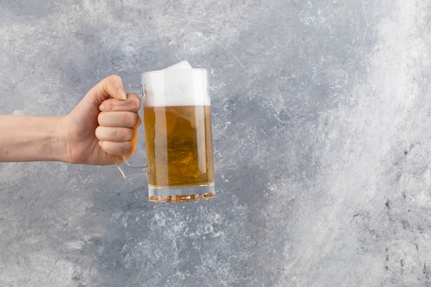 Male hand holding glass mug of beer with foam on stone surface