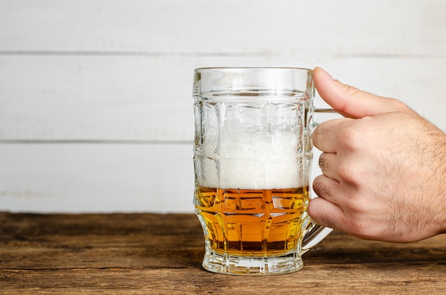 Male hand holding a half full beer glass with foam on wooden table