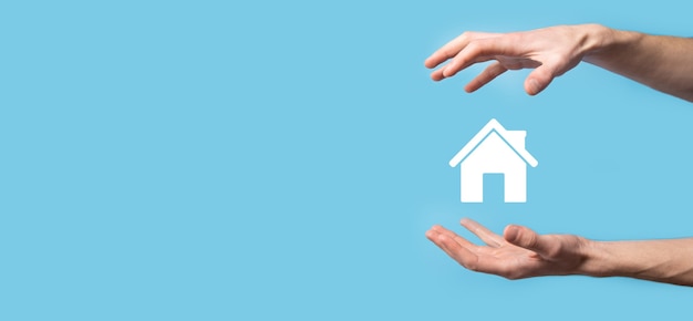 Male hand holding house icon on blue background