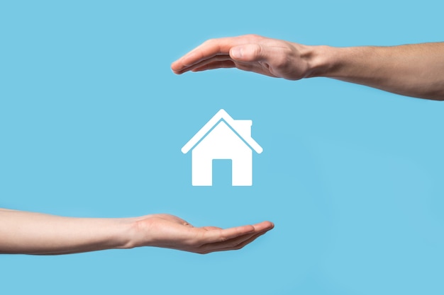 male hand holding house icon on blue background.
