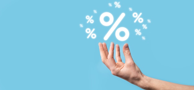 Mano maschio che tiene l'icona percentuale del tasso di interesse su sfondo blu. concetto di tassi finanziari e ipotecari di tasso di interesse. banner con spazio di copia