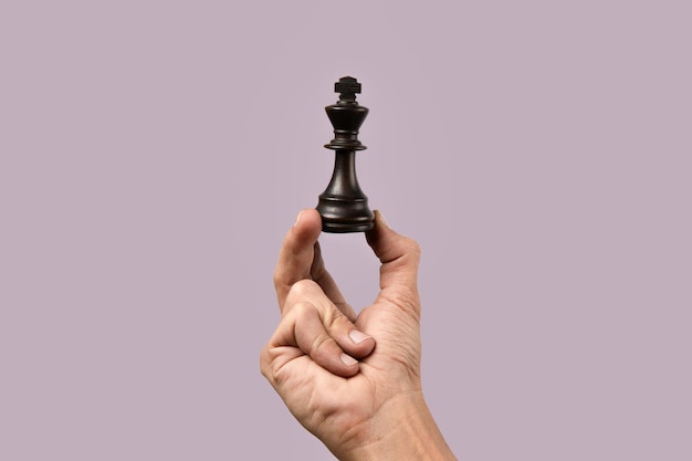 Фото Мужская рука держит шахматную фигуру короля на фиолетовом фоне