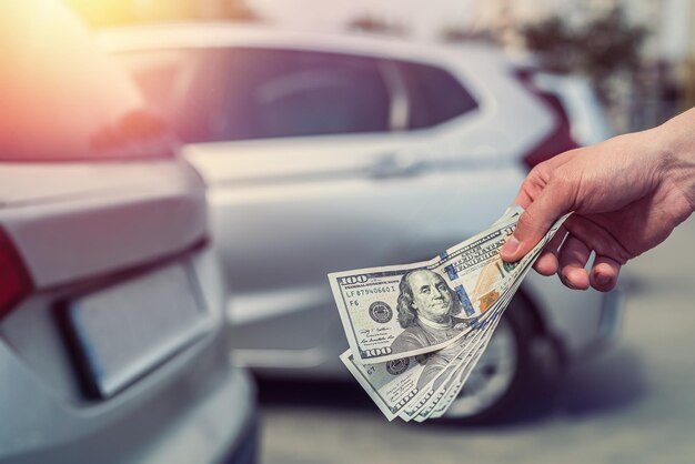 Male hand holding a lot of dollars against gray car in the back