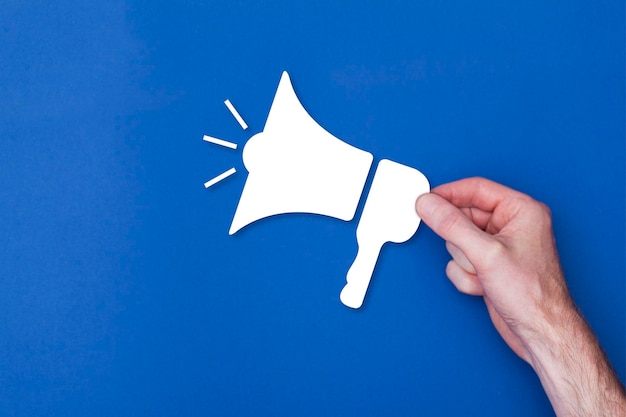 Male hand holding a loud speaker icon symbol against a blue background