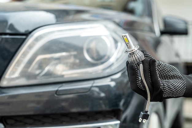 Male hand holding modern LED h7 bukb near headlamp of a car