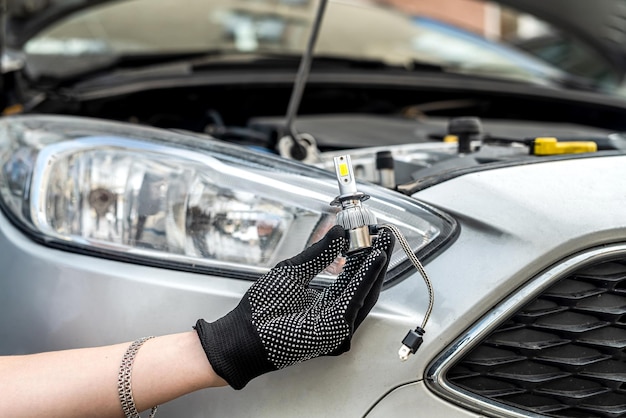 Male hand holding modern LED h7 bukb near headlamp of a car