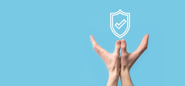 Photo male hand holding protect shield with a check mark icon on blue background. protection network security computer and safe your data concept .