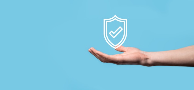 Male hand holding protect shield with a check mark icon on blue background. Protection network security computer and safe your data concept .