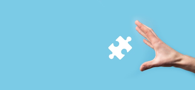 Male hand holding puzzle icon on blue surface