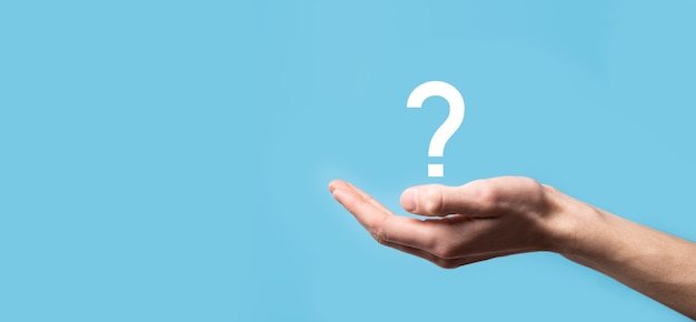 Male hand holding question mark icon on blue surface