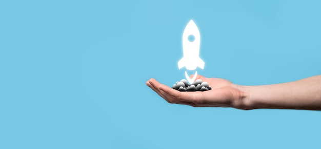 Male hand holding rocket icon that takes off, launch on blue
background. rocket is launching and flying out, business start up,
icon marketing on modern virtual interface.start up concept.