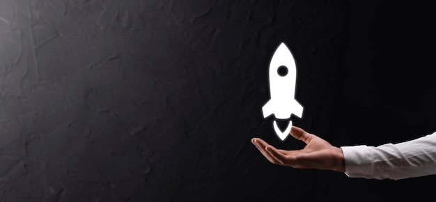 Male hand holding rocket icon that takes off, launch on blue background. rocket is launching and flying out, Business start up, Icon marketing on modern virtual interface.Start up concept.