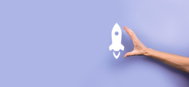 Male hand holding rocket icon that takes off, launch on blue background. rocket is launching and flying out, Business start up, Icon marketing on modern virtual interface.Start up concept.