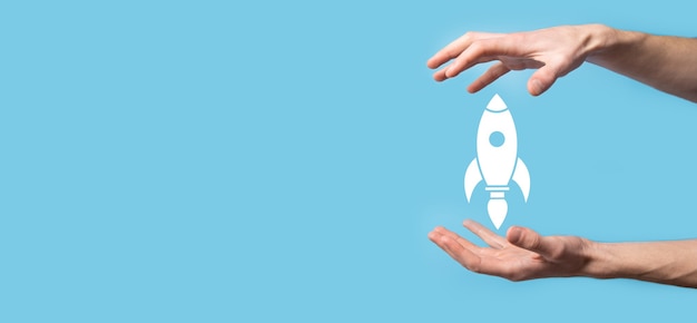 Male hand holding rocket icon that takes off, launch on blue\
background. rocket is launching and flying out, business start up,\
icon marketing on modern virtual interface.start up concept.