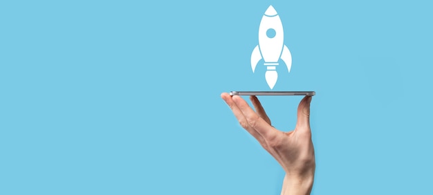 Male hand holding rocket icon that takes off, launch on blue background. rocket is launching and flying out, Business start up, Icon marketing on modern virtual interface. Start up concept.