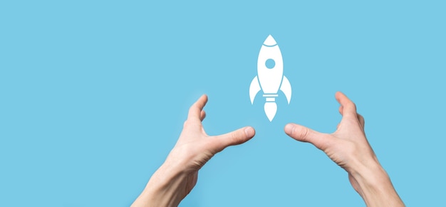 Male hand holding rocket icon that takes off, launch on blue background. rocket is launching and flying out, Business start up, Icon marketing on modern virtual interface.Start up concept.