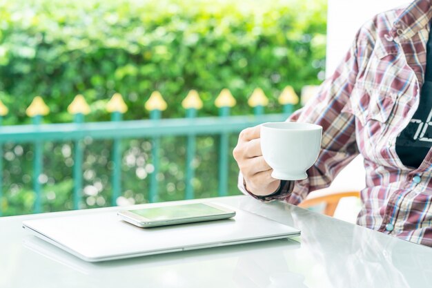 Male hand holding smart phone and cup of coffee on the table  