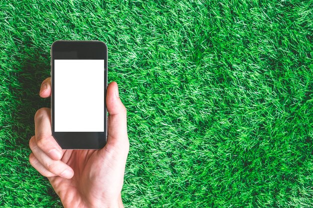 Male hand holding smart phone on green grass background. Free space for text