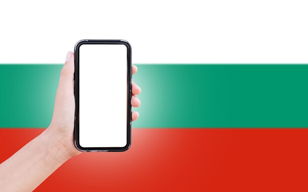 ブルガリアのクローズ アップ ビューのぼやけた旗の背景に画面に空白のスマート フォンを持っている男性の手