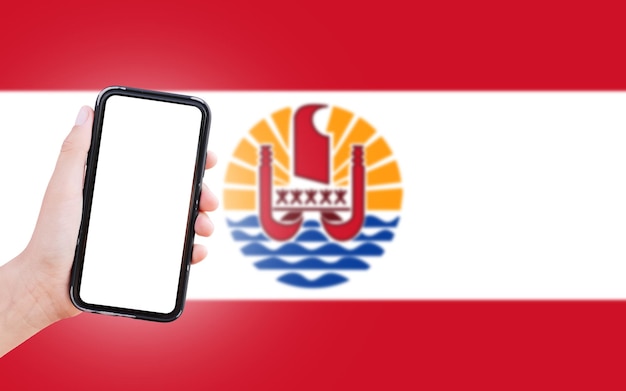 Male hand holding smartphone with blank on screen on background of blurred flag of French Polynesia Closeup view