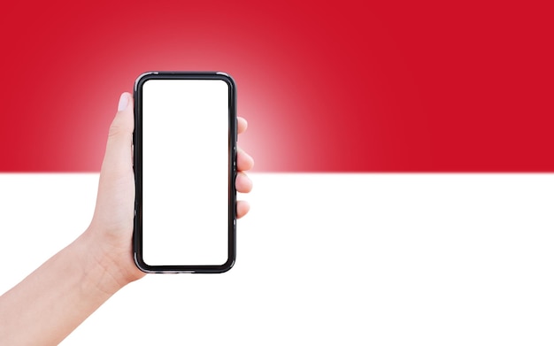 Male hand holding smartphone with blank on screen on background of blurred flag of Monaco Closeup view