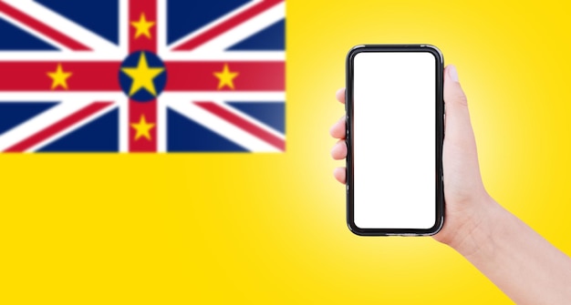 Male hand holding smartphone with blank on screen on background of blurred flag of Niue Closeup view