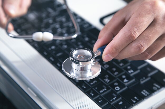 Male hand holding stethoscope on a laptop keyboard.