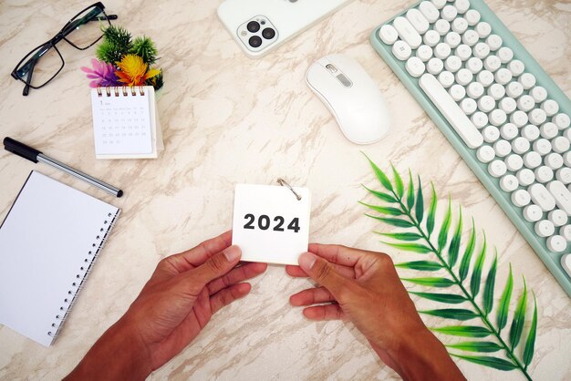 Male hand holding table calendar with white marble background Todo list and plans for 2024 Goals f