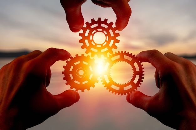 Male hand holding three wooden cog gear wheel on blue sky background. sunshine and yellow sky .