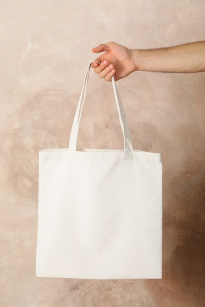 Male hand holding tote bag against brown background