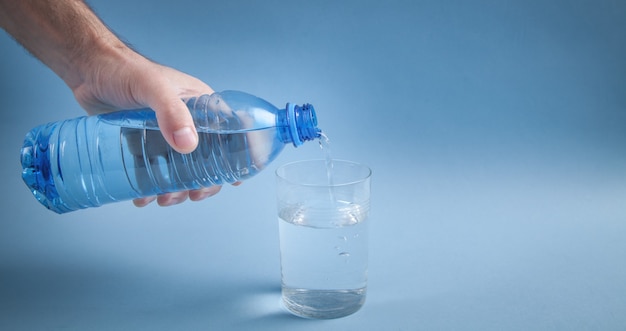 Male hand holding water bottle pouring water into glass.