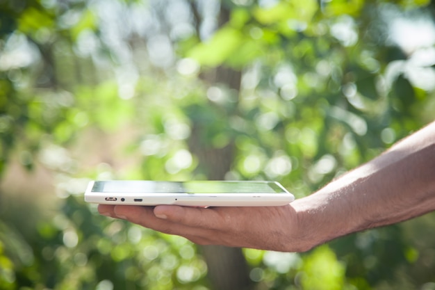 Male hand holding white digital tablet in nature.