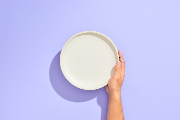 Male hand holding white plate, isolated on lilac