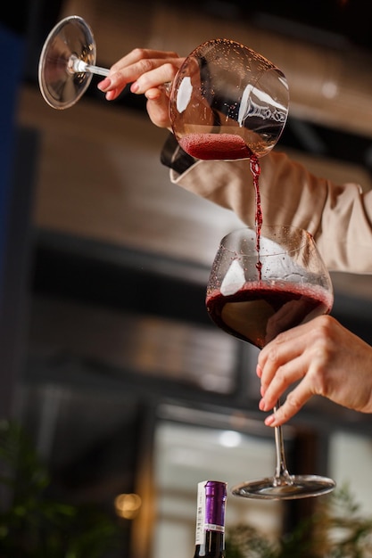 Foto la mano maschile tiene bellissimi calici trasparenti per vino bordeaux in cui il vino rosso viene versato da un altro calici