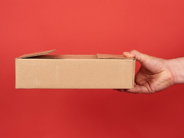 Male hand holds a brown cardboard box on a red background