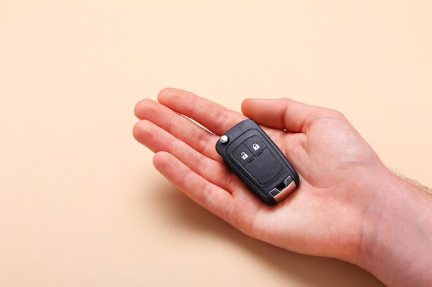 Male hand holds car keys on beige background. Concept car, car rental, gift, driving lessons, driving license. Flat lay, top view